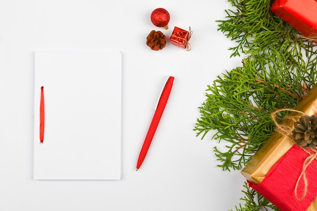 Blank white notebook and red pen on christmas white space. Christmas fir branches, cones, gifts. Letter to Santa Claus, mock up. Blank white notebook and red pen on white.