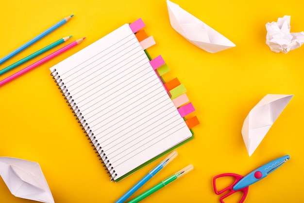 Blank white notepad with papers pencils and scissors on yellow background