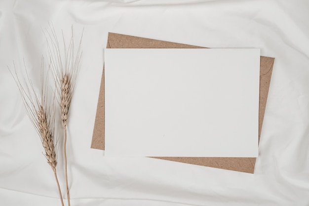 Blank white paper on brown paper envelope with Barley dry flower on white cloth