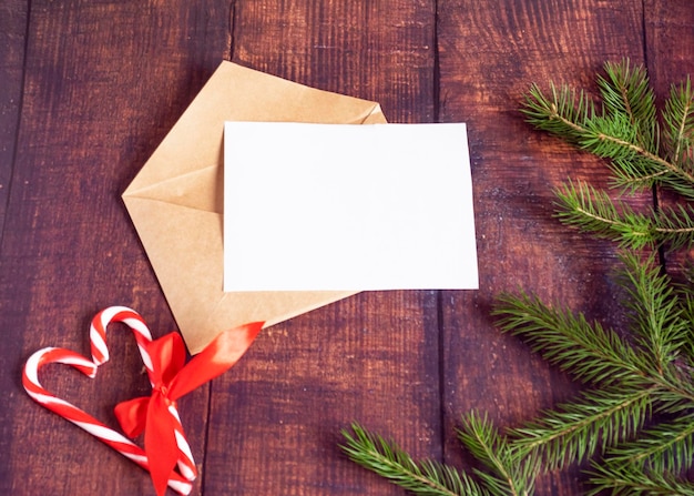 Blank white paper card in a brown envelope from handmade craft paper on an old wooden table in a Christmas style Fir branches cones on the table