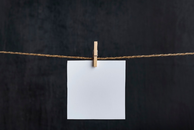 Blank white paper card hang with clothespins on rope on black background. Copy space. Place for your text.