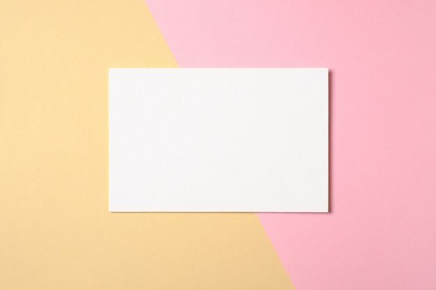 Blank white paper card on two color pastel pink and yellow background.