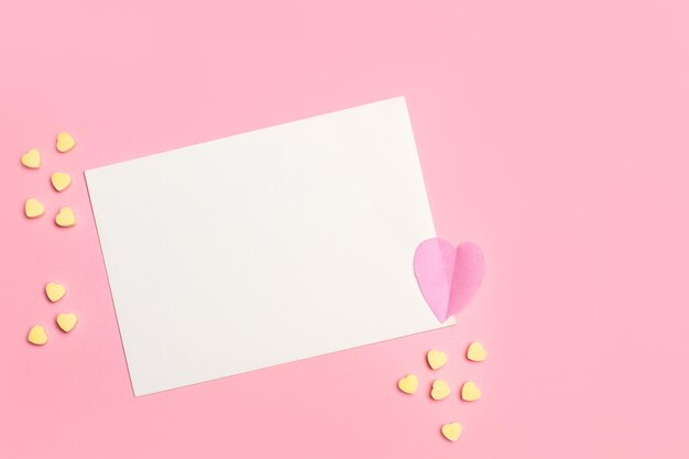 a blank white paper card with copy space and yellow candy hearts on a pink background