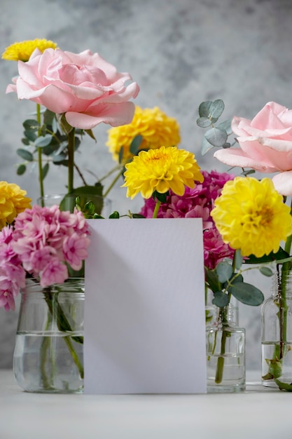 Blank white paper greeting card mock up Pink and yellow flowers in vases with copy space Hydrangea dahlias and eucalyptus