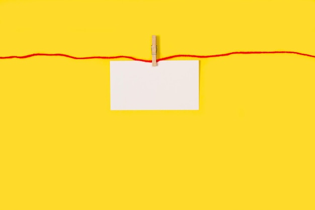 Blank white paper hanging from a red thread on a yellow background