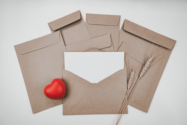 空白の白い紙は、赤いハートと大麦ドライフラワーと開いた茶色の紙の封筒に置かれます