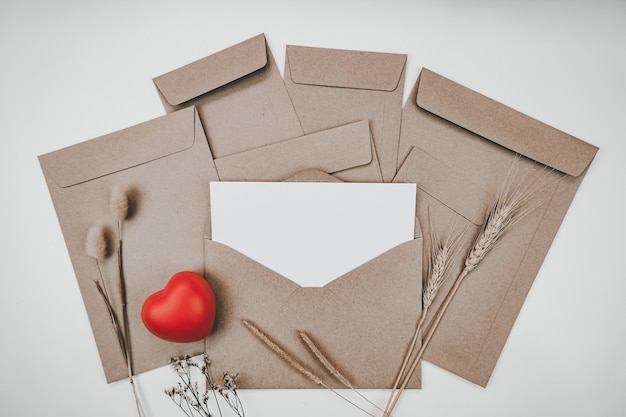 Blank white paper is placed on open brown paper envelope with red heart, Many kinds of dried flowers