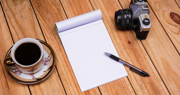 Note di carta bianca in bianco con caffè e vecchia macchina fotografica sulla tavola di legno superiore