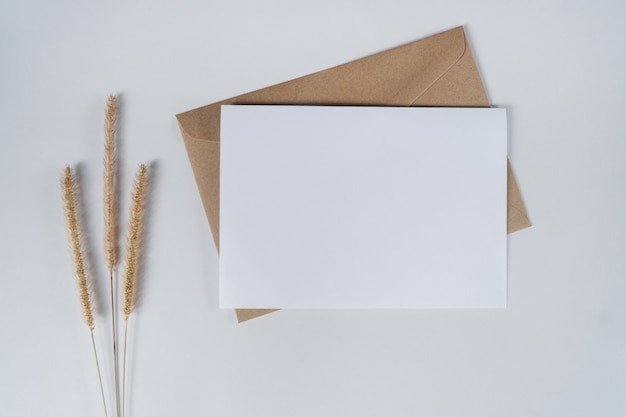 Чистый белый лист на коричневом бумажном конверте с щетинистым сухим цветком. вид сверху конверта из крафт-бумаги на белом фоне.