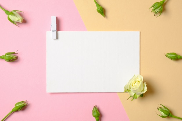 Photo blank white paper with clothespin and flowers on pink and yellow background.