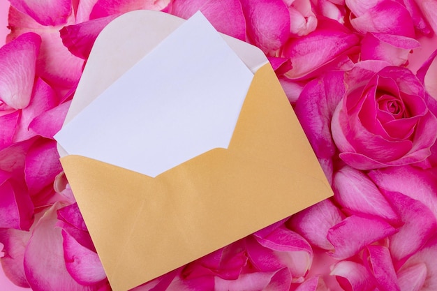 Blank white paper with copy space in envelope on fresh aromatic pink rose petals and flowers