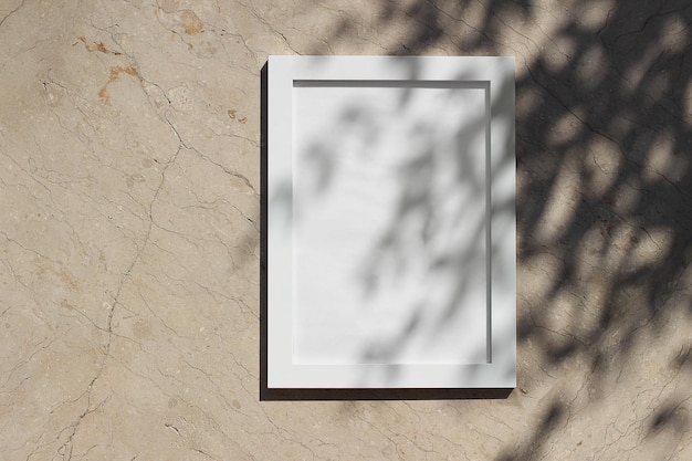 Blank white picture frame against beige marble background in sunlight Dark tree leaves branches silhouettes overlay harsh shadows Empty poster mockup for art display Minimal summer design