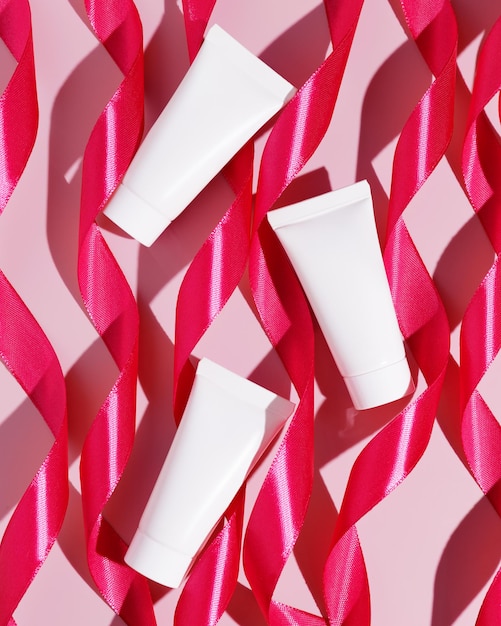 Blank white plastic cosmetic tubes with pink ribbons Cosmetic beauty product branding mockup