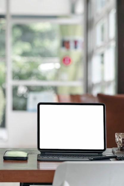 Blank white screen tablet with magic keyboard on wooden table in modern living room, vertical view.