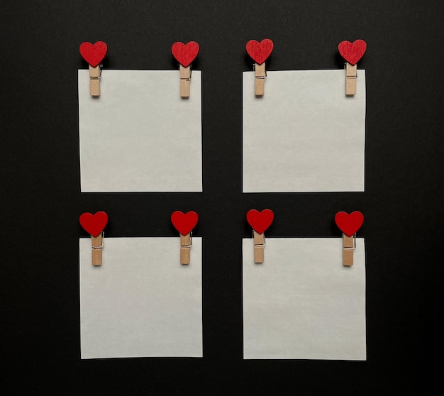 blank white stickers, wooden clothespins with red hearts on black background, top view.