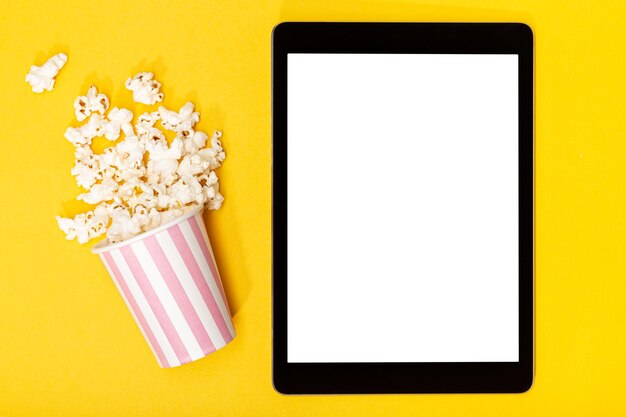 Blank wit scherm tablet en popcorn emmer op gele achtergrond Template mockup Top view