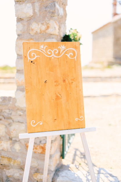 Photo blank wooden easel with monograms stands near a stone column on a stand