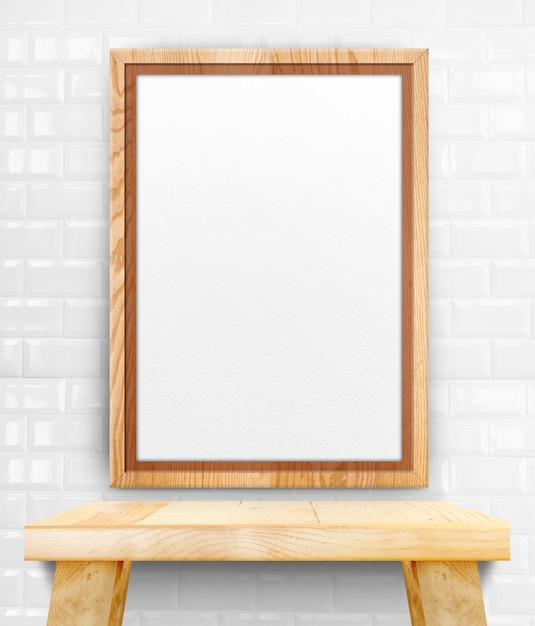 Blank wooden photo frame hanging at white tile wall on wood table.