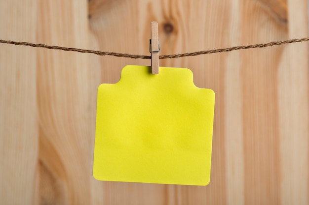 Photo blank yellow paper card hang with clothespin on rope. place for your text. copy space. wooden background.