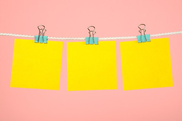 Blank yellow paper note hanging on clothesline over pink background