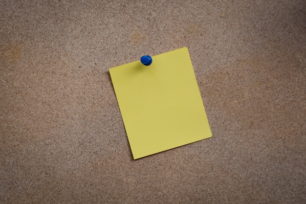 Blank yellow paper note pinned on cork board with white thumbtacks, copy space available