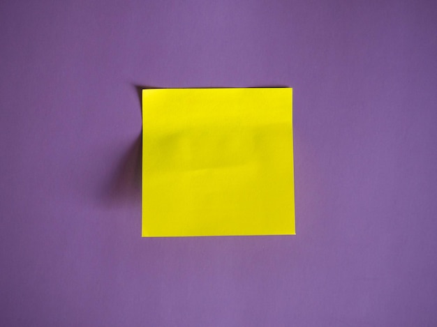 Adesivo di carta giallo vuoto per note e penna su sfondo viola