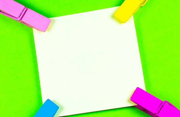 Blank yellow sticker with colorful wooden clothespins. Close up of note paper on green background. Copy space.