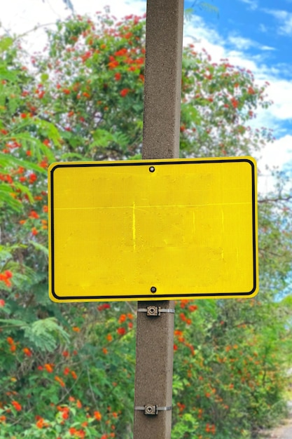 blank yellow warning sign board on flower bush background