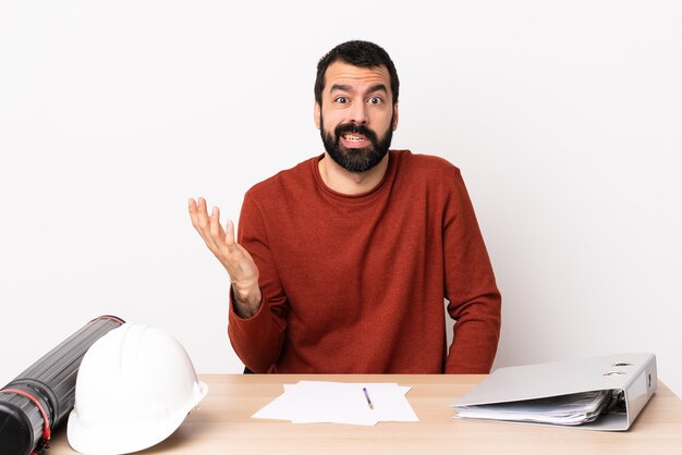 Blanke architect man met baard in een tafel twijfels gebaar maken.