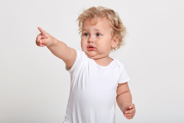 Blanke baby wijst met wijsvinger weg, ziet iets interessants, draagt een t-shirt