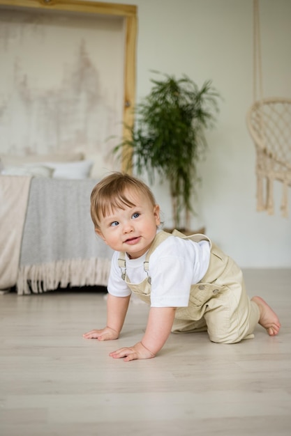 Blanke babyjongen met een scheel in een beige jumpsuit kruipt op de vloer in de slaapkamer ontwikkeling van het kind