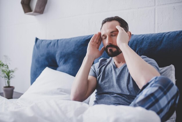 Blanke bebaarde man met hoofdpijn zittend op bed