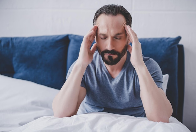 Blanke bebaarde man met hoofdpijn zittend op bed