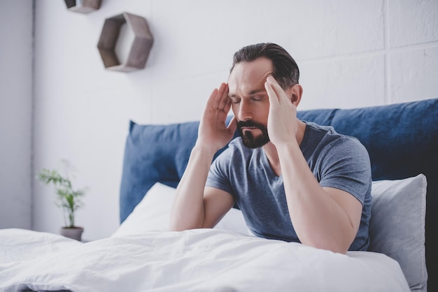 Blanke bebaarde man met hoofdpijn zittend op bed