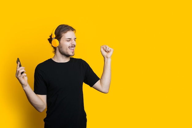 Blanke bebaarde man met koptelefoon en lang haar danst op een gele muur met lege ruimte