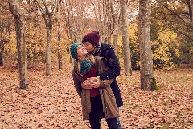 Blanke blanke man knuffelt zijn vriendin van achteren en kust haar in een park in de herfst