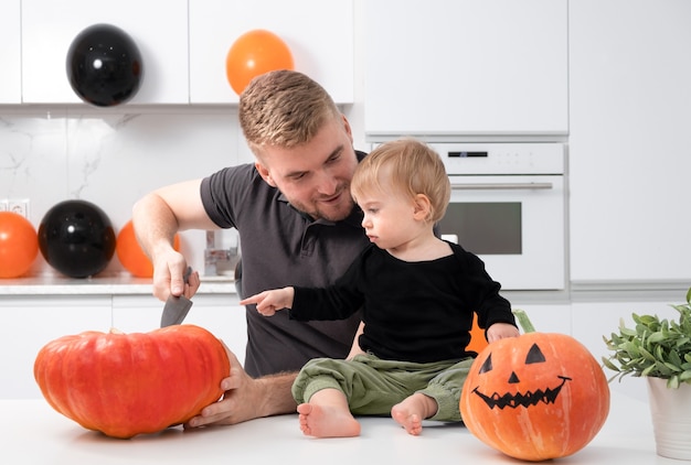 Blanke blonde man snijdt een schattige baby die op tafel zit Fijne Halloween-dag met familie