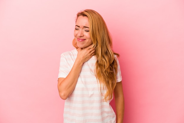 Blanke blonde vrouw geïsoleerd op roze achtergrond lijdt aan pijn in de keel als gevolg van een virus of infectie.