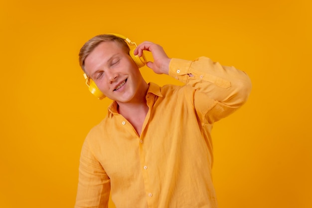 Blanke blondine op een gele achtergrond met draadloze koptelefoon die naar muziek luistert