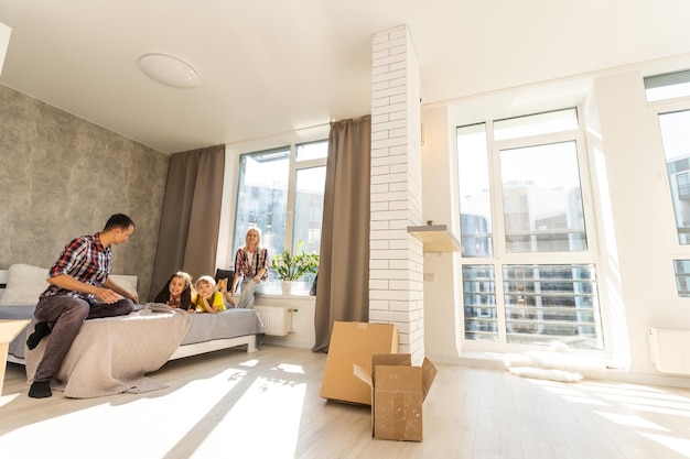 Blanke familie, man, vrouw en twee meisjes zitten op de vloer, pakken dozen uit en glimlachen in het nieuwe huis. daarachter verhuisdozen.