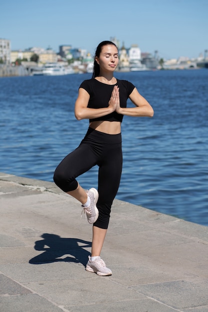 Blanke gebruinde brunette vrouw die yoga beoefent aan de rivier