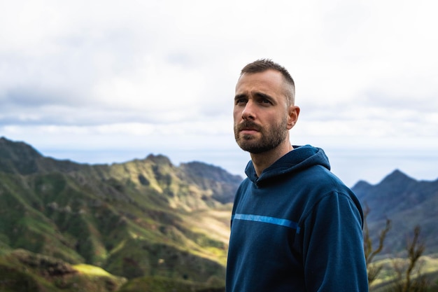 Blanke jonge aantrekkelijke man met blauwe hoodie op een bewolkte dag die serieus naar het landschap kijkt