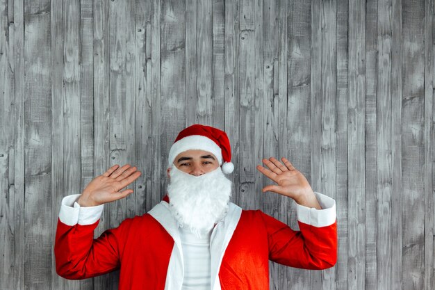 Foto blanke jonge man verkleed als kerstman met handen omhoog. ruimte bovenaan kopiëren