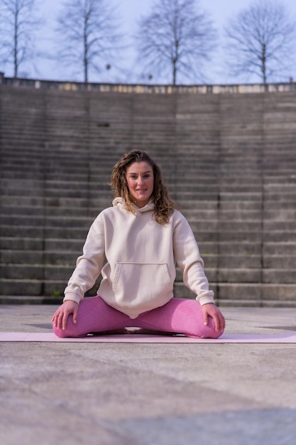 Blanke jonge vrouw doet fitness in een stadspark en warmt pre-oefening op de mat op