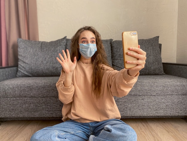 Blanke jonge vrouw, gekleed in een medisch masker om thuis te zitten op zelfisolatie tijdens de coronavirus pandemie.