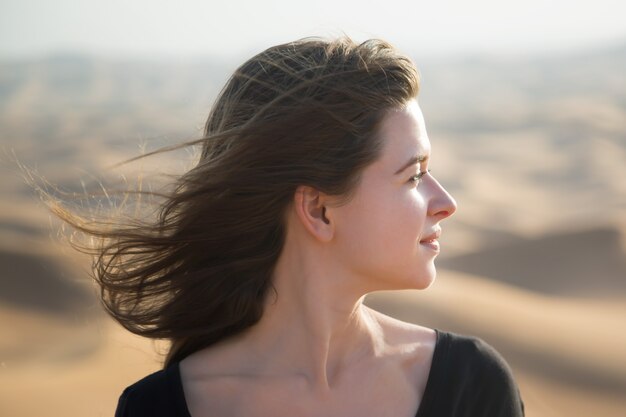Blanke jonge vrouw met lang haar in een zwarte jurk bij zonsopgang in de woestijn