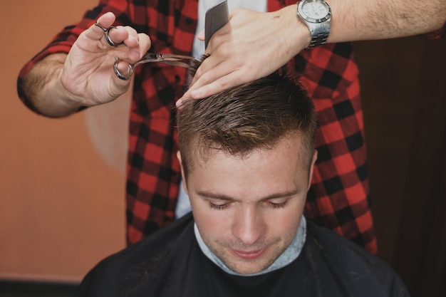 Blanke jongeman in Barbershop Kapper knipt zijn haar in hipsterstijl