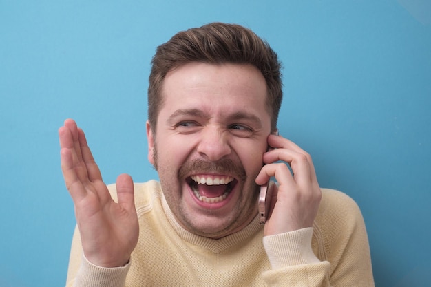 Foto blanke jongeman pratend door smartphone glimlachend en lachend gelukkig onder de indruk van nieuws