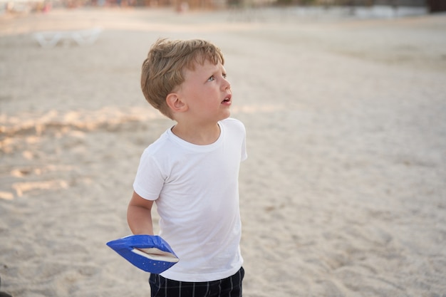 Blanke jongen permanent strand. Jeugd zomer. Familievakantie met één kind. Knap klein kind met speelgoed handgemaakt schip