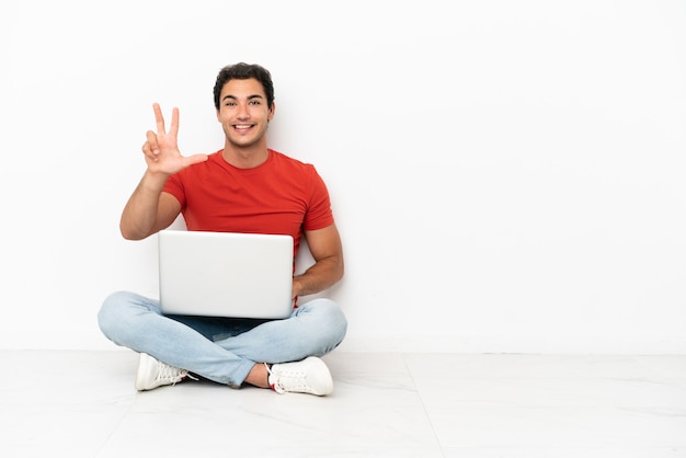 Blanke knappe man met een laptop die blij op de grond zit en drie telt met vingers